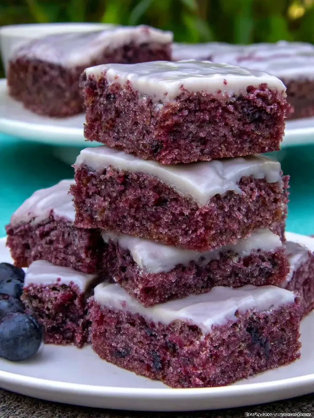 A stack of brownies with white icing and blueberries.