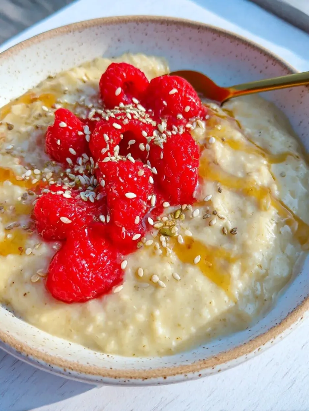 A bowl of creamy custard oatmeal with raspberries on top.