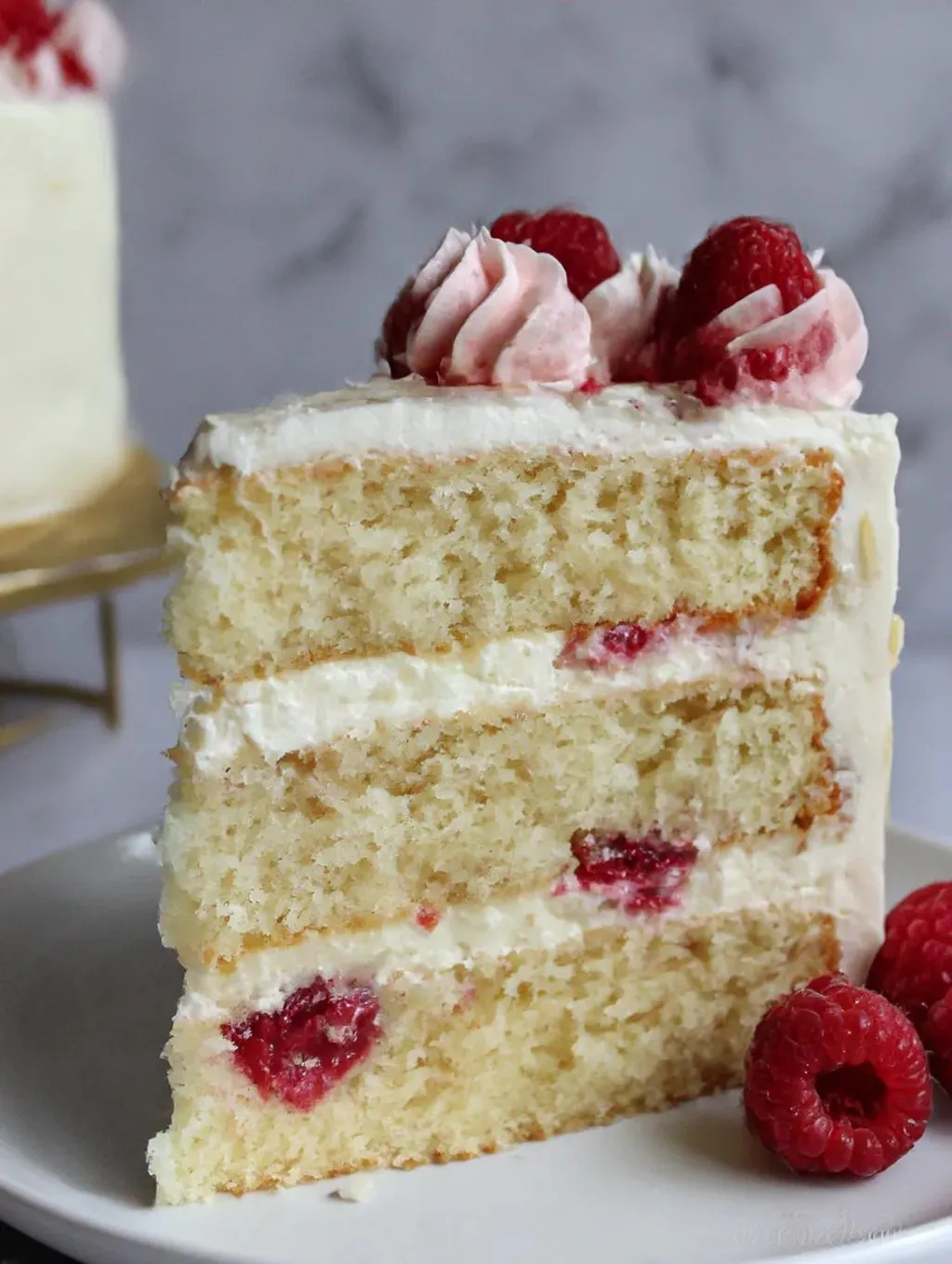 A slice of a coconut cake with raspberries on top.