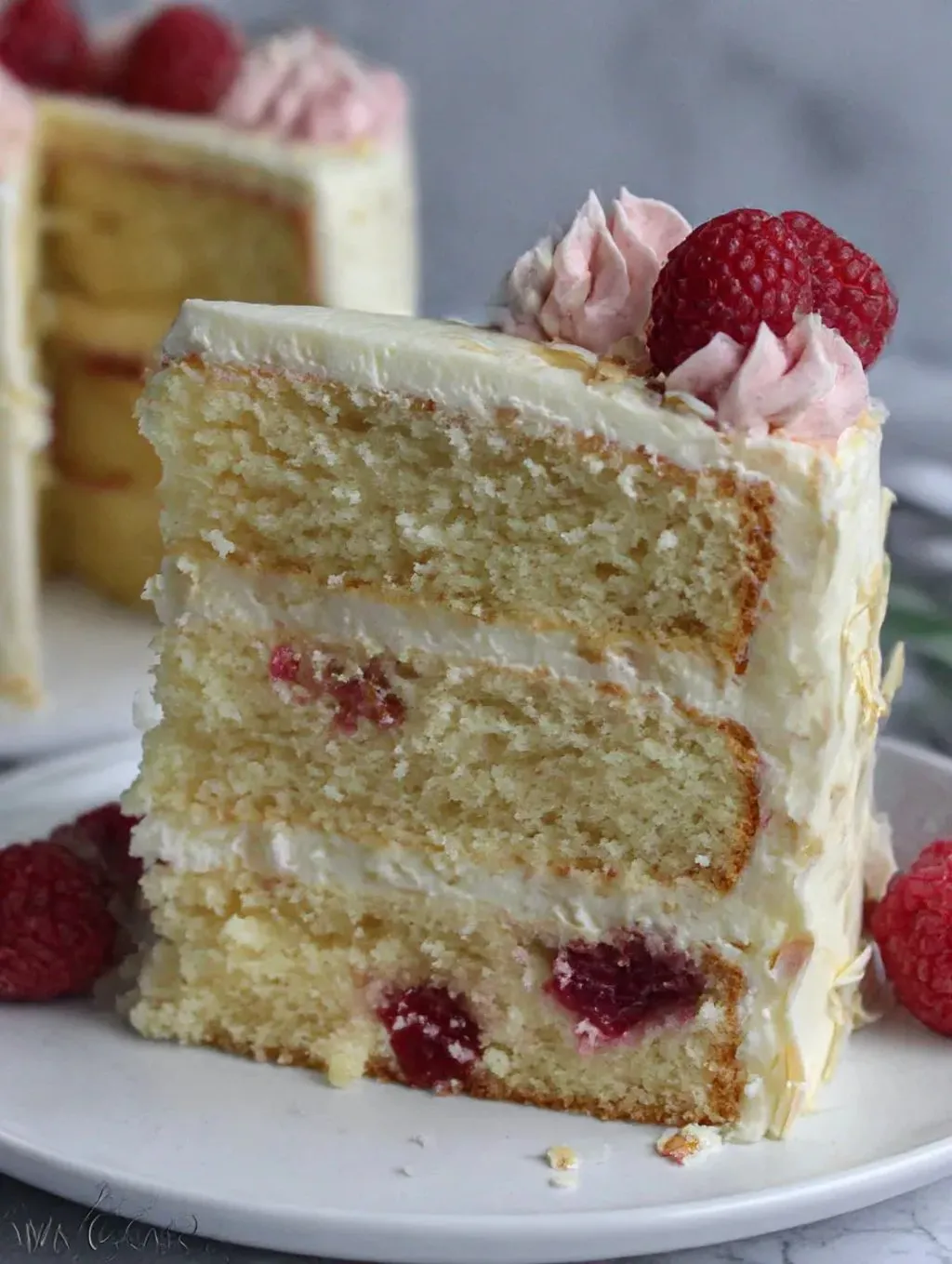 A slice of coconut cake with raspberries on top.