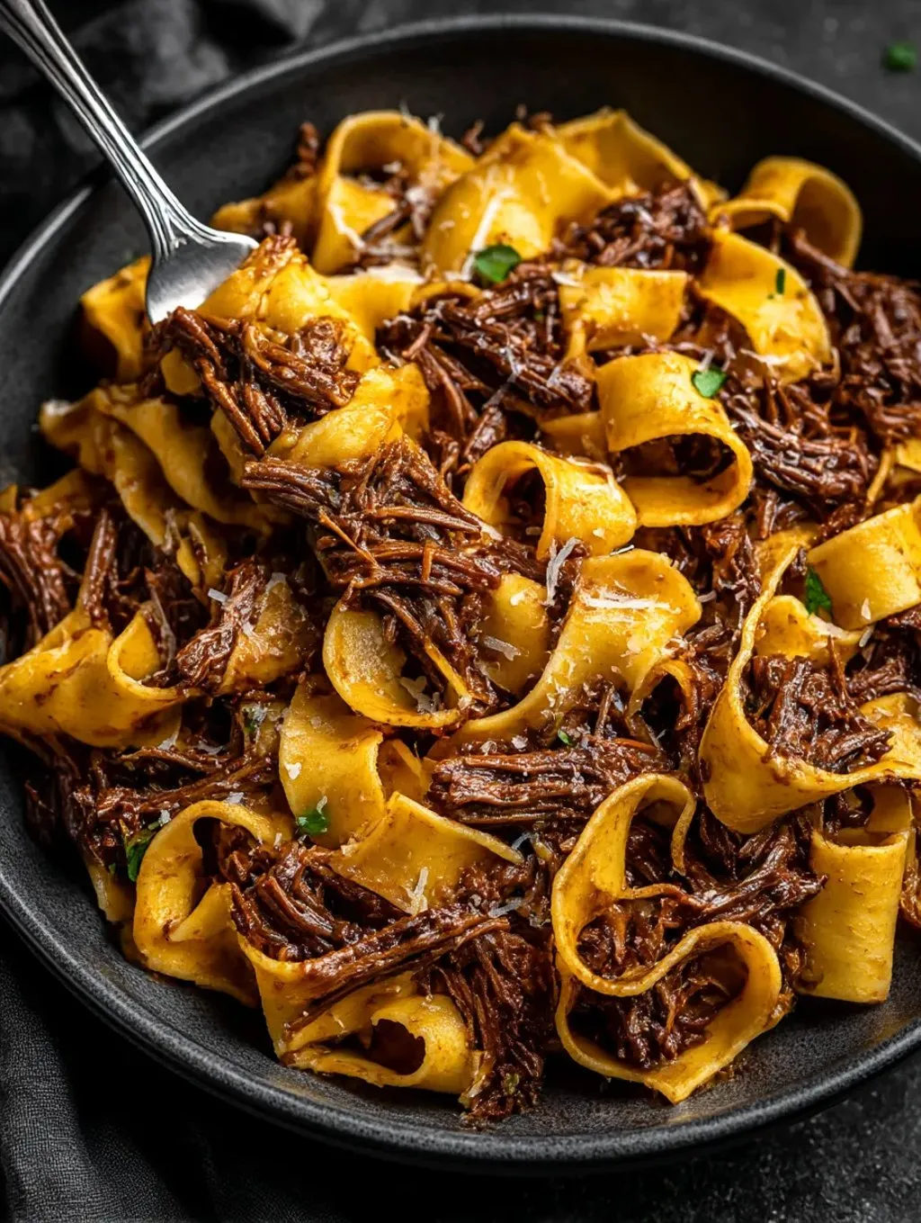 A bowl of short ribs with a fork in it.